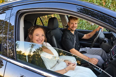 Los novios sonríen desde el coche a la luz del atardecer, ella de blanco en el asiento del copiloto