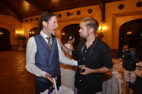 El novio conversa animado con el fotógrafo durante el convite, con la novia al fondo
