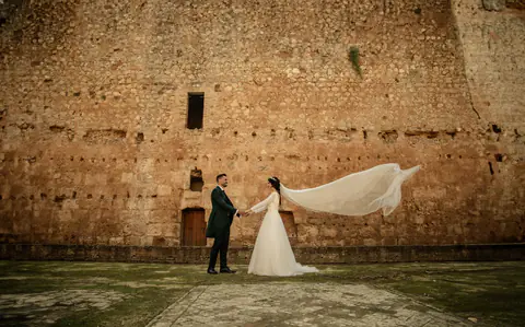 The couple in front of a stone wall, the veil spread out by the wind